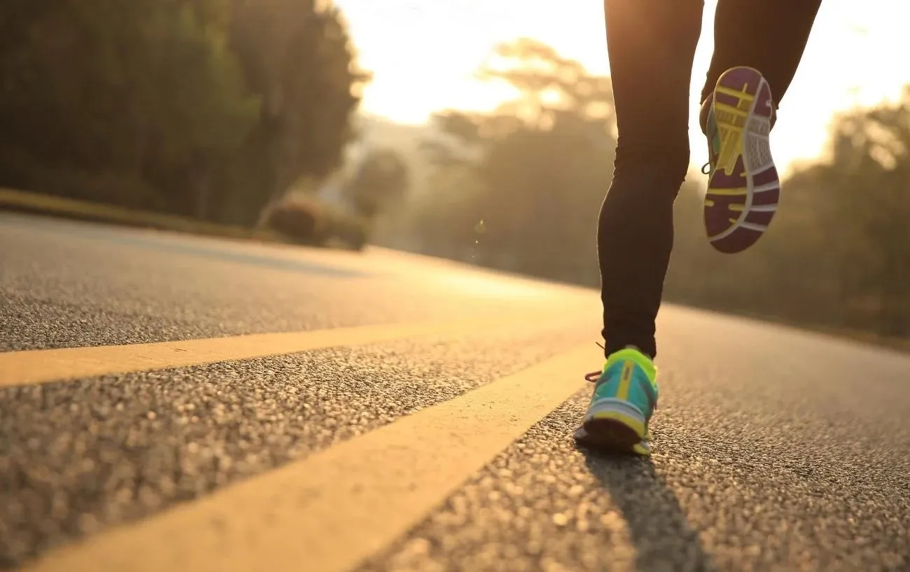 бегун's shoes as a runner runs down the middle of a road with nice light