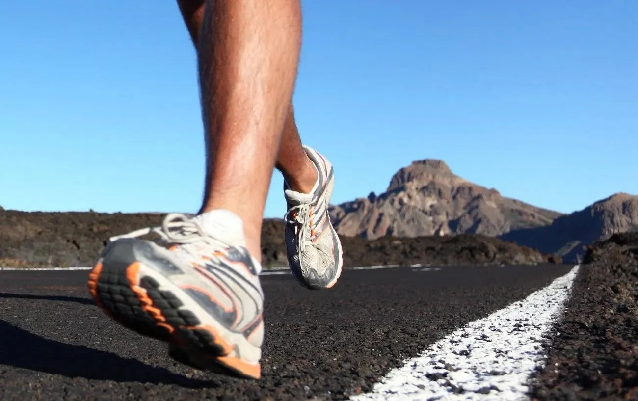 Крупный план человека's running shoes as they run on an asphalt road.