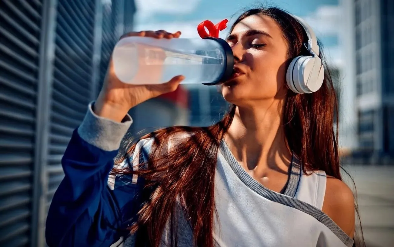 Человек в наушниках пьет воду из бутылки.