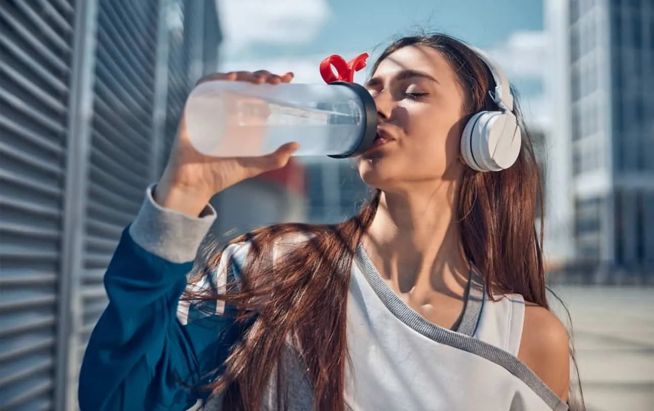 Женщина пьет воду после тренировки. 