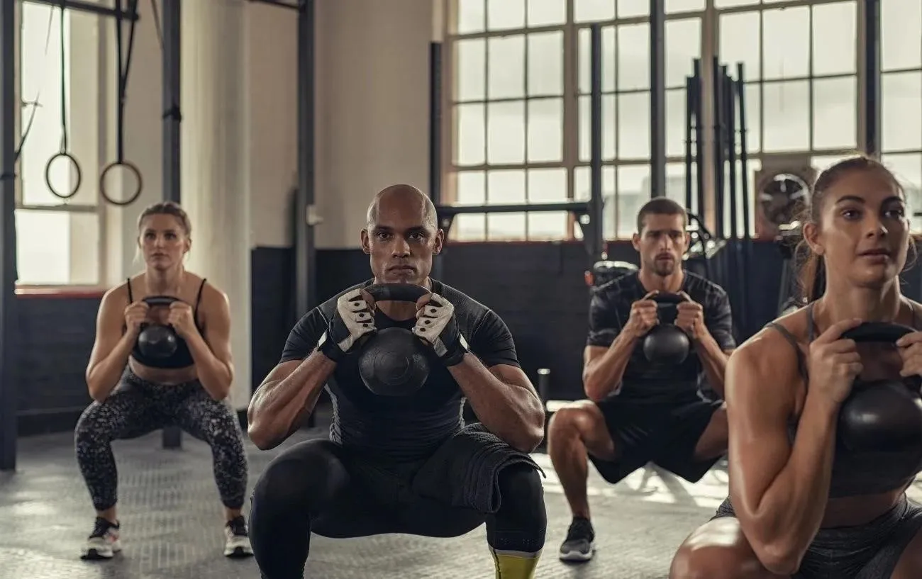 Класс CrossFit, где люди выполняют приседания с гантелями.