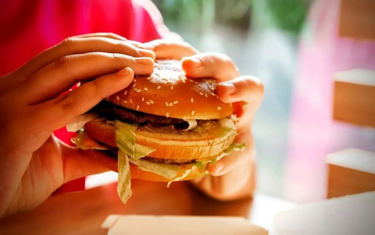 Человек ест гамбургер из Mcdonalds. 