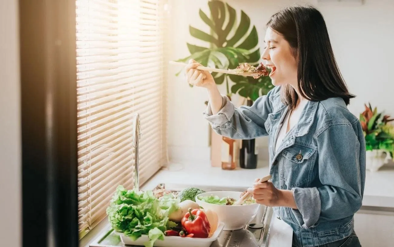 Человек готовит салат и откусывает кусочек.