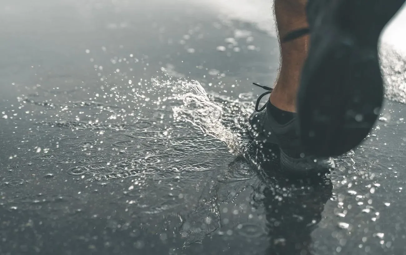 Крупный план человека's running sneakers as tey go through a puddle.